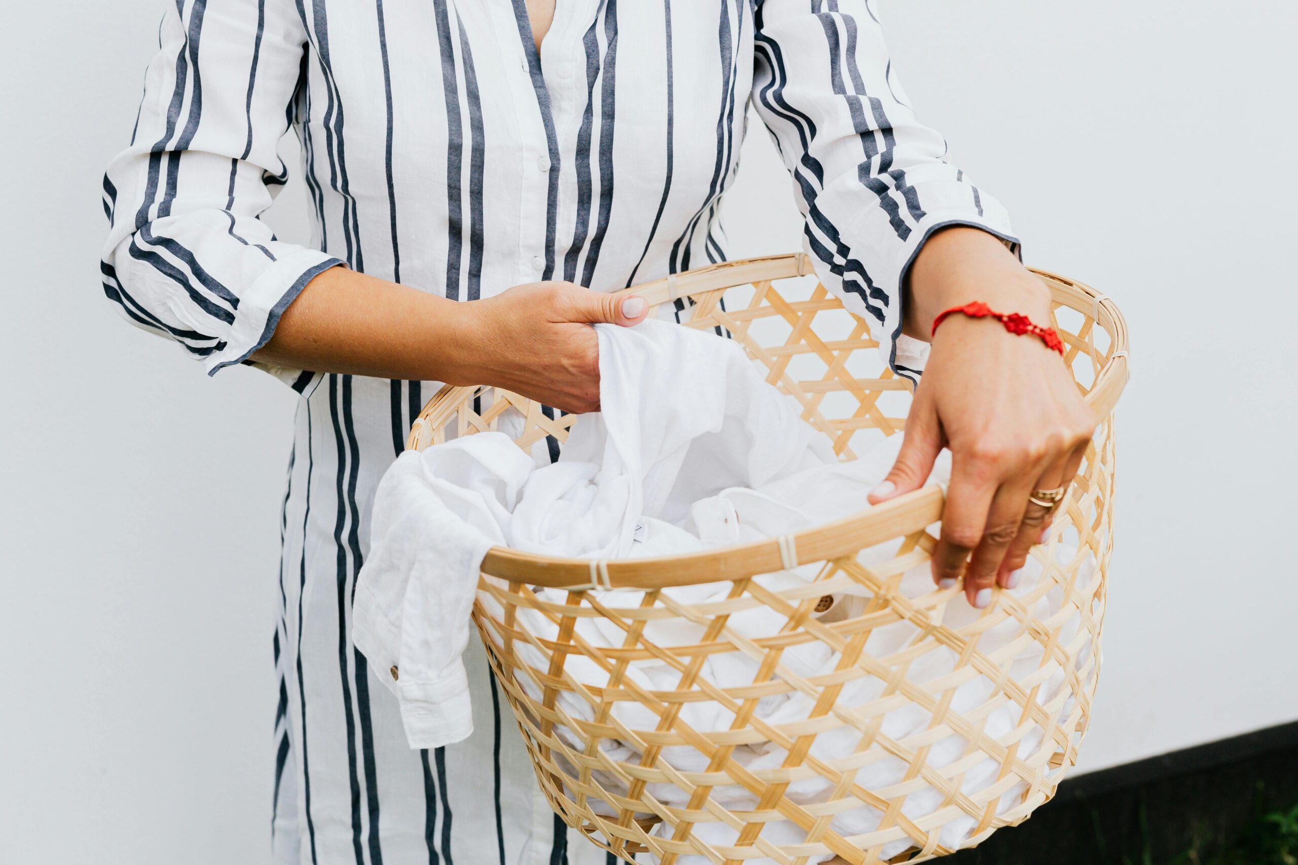 A woman holds a wicker laundry basket with white clothes indoors.
